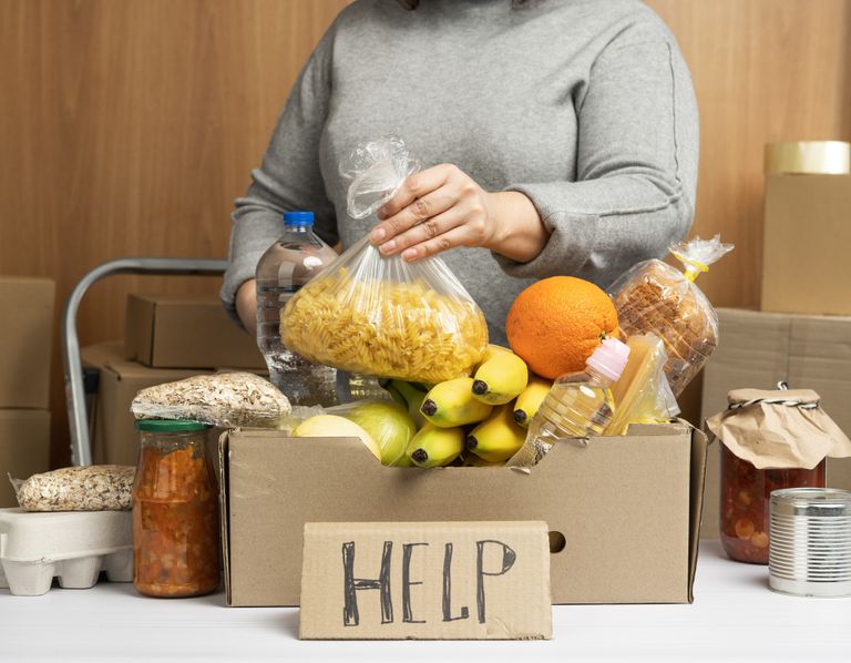 An image of a woman putting food in a box with a cardboard sign in front with the text help.