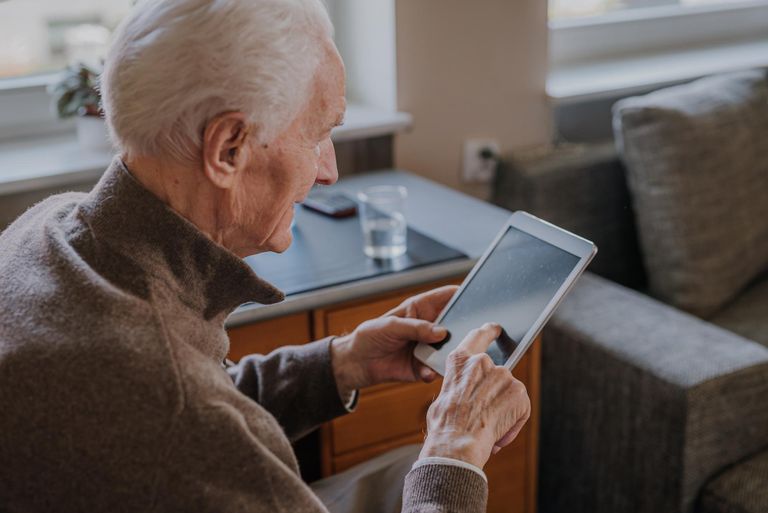 An eldery man sits on his couch and is using his tablet computer