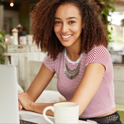 A smiling young woman in front of her computer with a cup of coffee. 