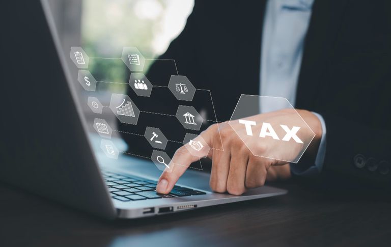 A person sitting at a desk with laptop. hand on laptop keyboard . a graphic overlay of various icons and text floats over, one saying tax.