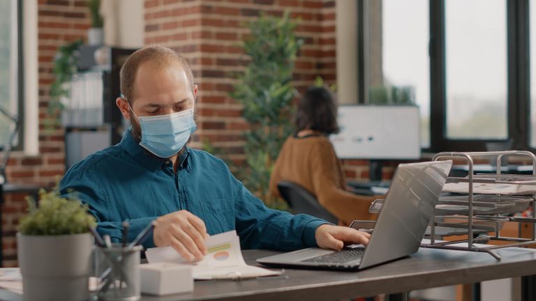 A man sitting at a desk working while wearing a surgical mask