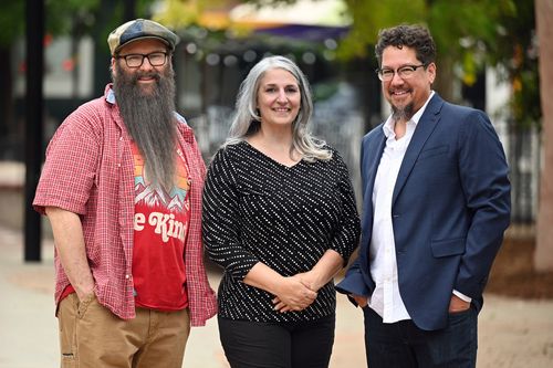 Group photo of the Ridiculous Engineering founders, featuring Patrick Lanigan, Patrizia Marziali, and Paul Ramos, smiling and standing outdoors. Patrick is wearing a cap and a red checkered shirt with a long beard, Patrizia is wearing a black and white patterned top with long gray hair, and Paul is wearing glasses, a blue suit, and a white shirt.