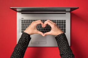 Overhead photo of grey laptop and hands with gesture as heart isolated on the red backdrop