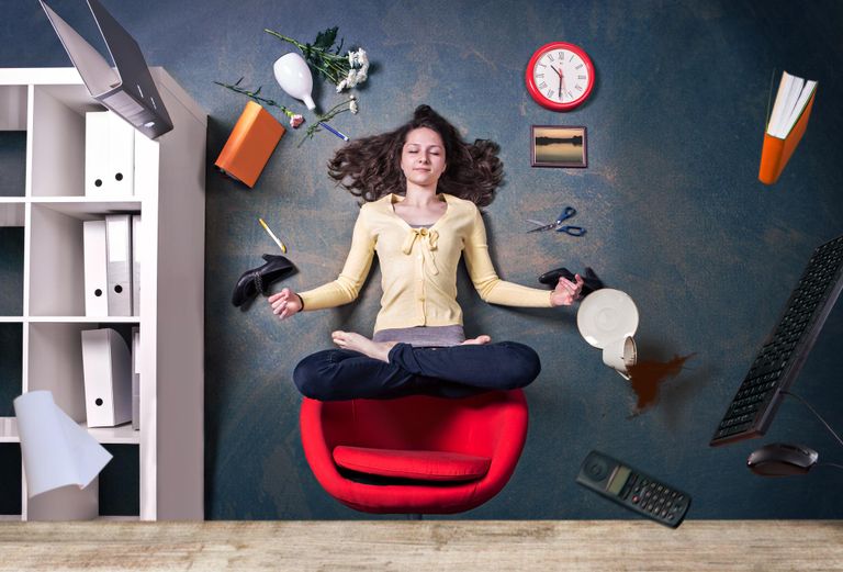 A woman floating above her desk char in a lotus position with office supplies floating around her.