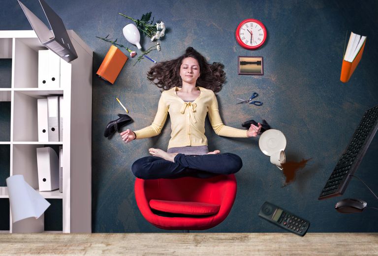 A woman floating above her desk char in a lotus position with office supplies floating around her.